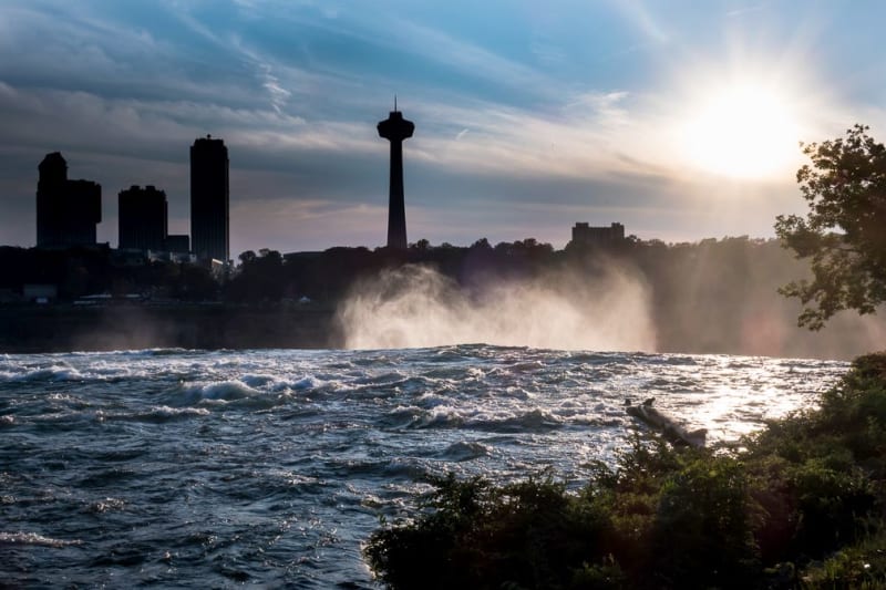 The skyscrapers on the Canadian side of the falls are silhouetted by the setting sun. We view them from the US side, over the fast streaming falls.
