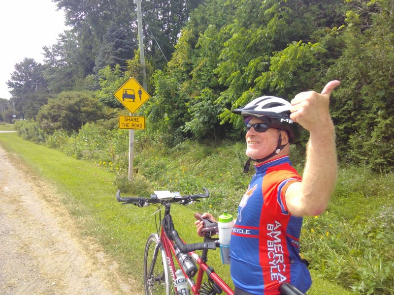 Chris gives a thumbs up in front of a sign reading "Share the road" with a picture of a car and a bicycle 